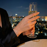 Thumbnail for Hand holding a champagne flute above a city skyline at night, wearing the Crystal Bar Bracelet