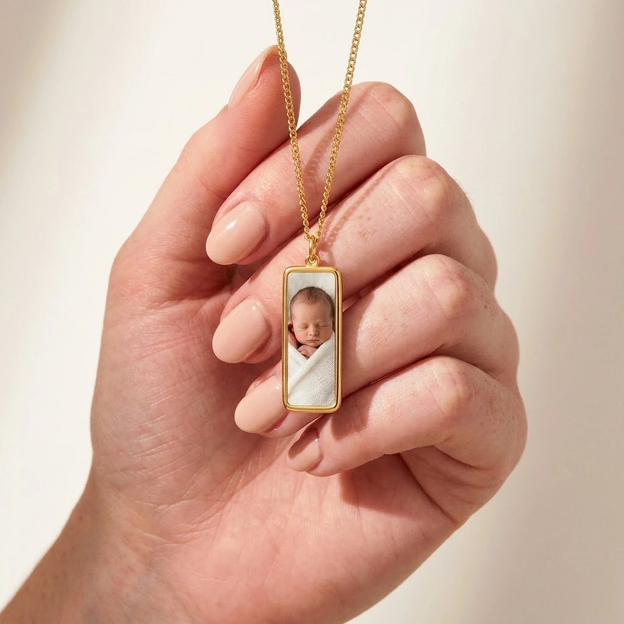 Gold bar pendant held between two fingers, real small size, newborn photo inside | SKU: TPH-BARN-GOLD